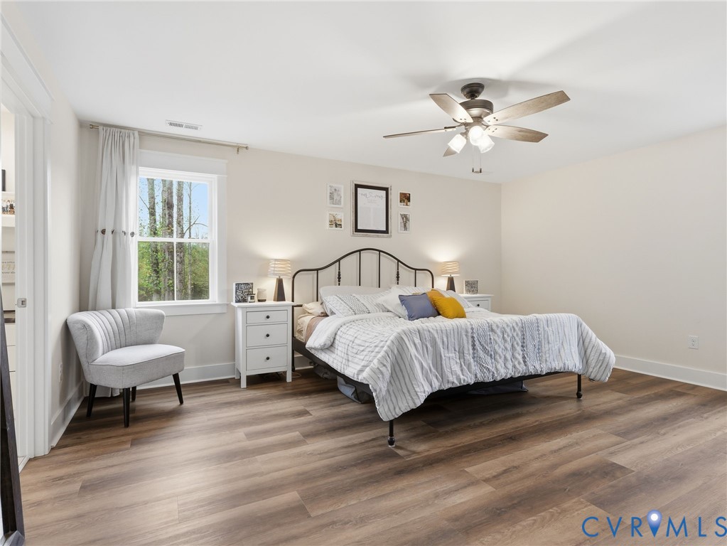 Bedroom featuring wood-finish flooring, a multi-blade ceiling fan with integrated lighting, and a window with exterior forest scenery
