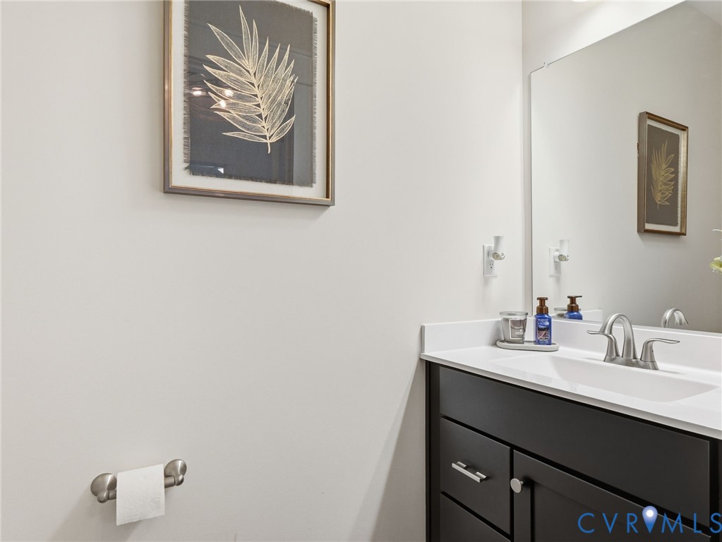 Dark-finished vanity with shaker-style cabinetry, white countertop, integrated basin, dual-handle brushed-nickel faucet, and large frameless wall mirror