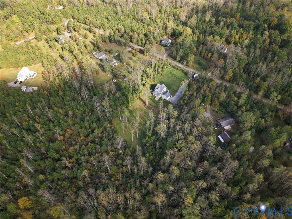 Aerial perspective of a sprawling parcel featuring dense mature woodland, expansive cleared acreage, a paved driveway, and detached storage structures
