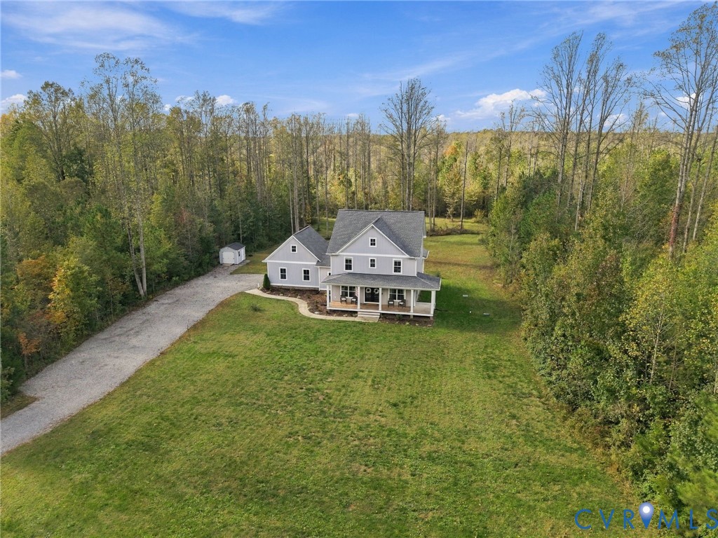Two-story home with light grey siding, a covered front porch, an attached side garage, a gravel driveway, and a detached outbuilding, all situated on a large lot surrounded by mature trees