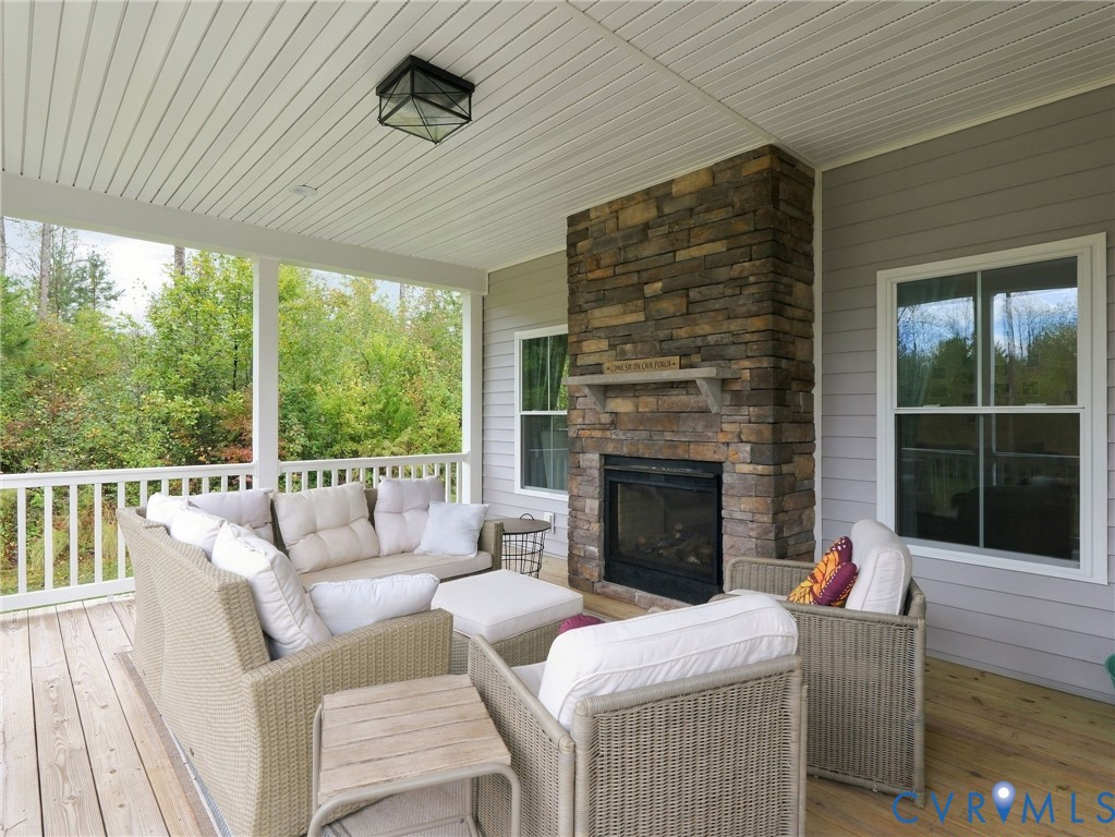 Covered porch featuring a wood-plank deck, stone-veneer fireplace with a wood mantel, paneled ceiling, and white railing