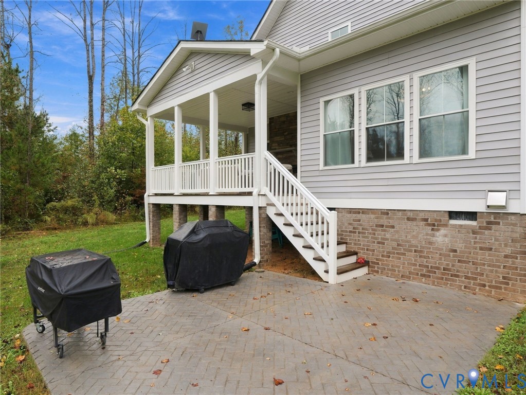 Covered back porch featuring light gray horizontal siding, a stone fireplace, white railings, and a stamped concrete patio