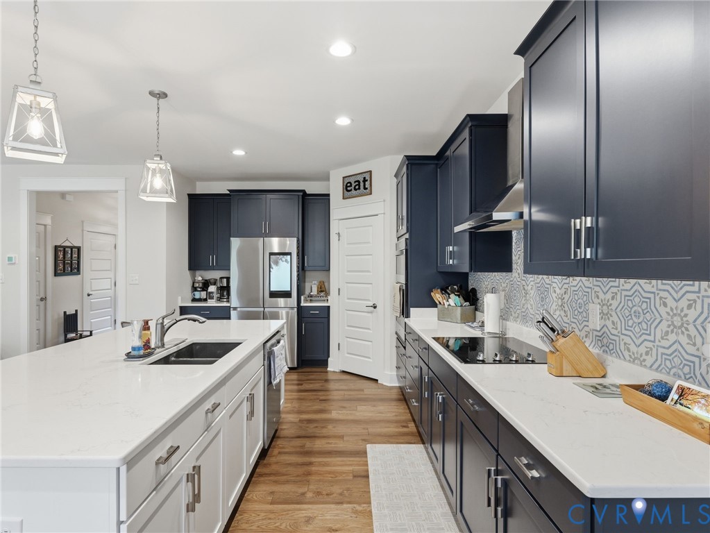 Kitchen featuring dark navy cabinetry, white quartz countertops, patterned tile backsplash, wood-finish flooring, and pendant lighting