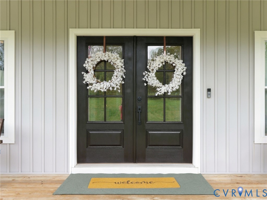 Double entry doors featuring six-light glass panels and dark finish hardware, set against light gray vertical board-and-batten siding