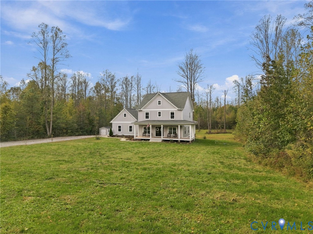 Two-story residence featuring grey lap siding, an expansive covered front porch, a multi-gabled roofline, and a detached outbuilding, all set on a large grassy lot