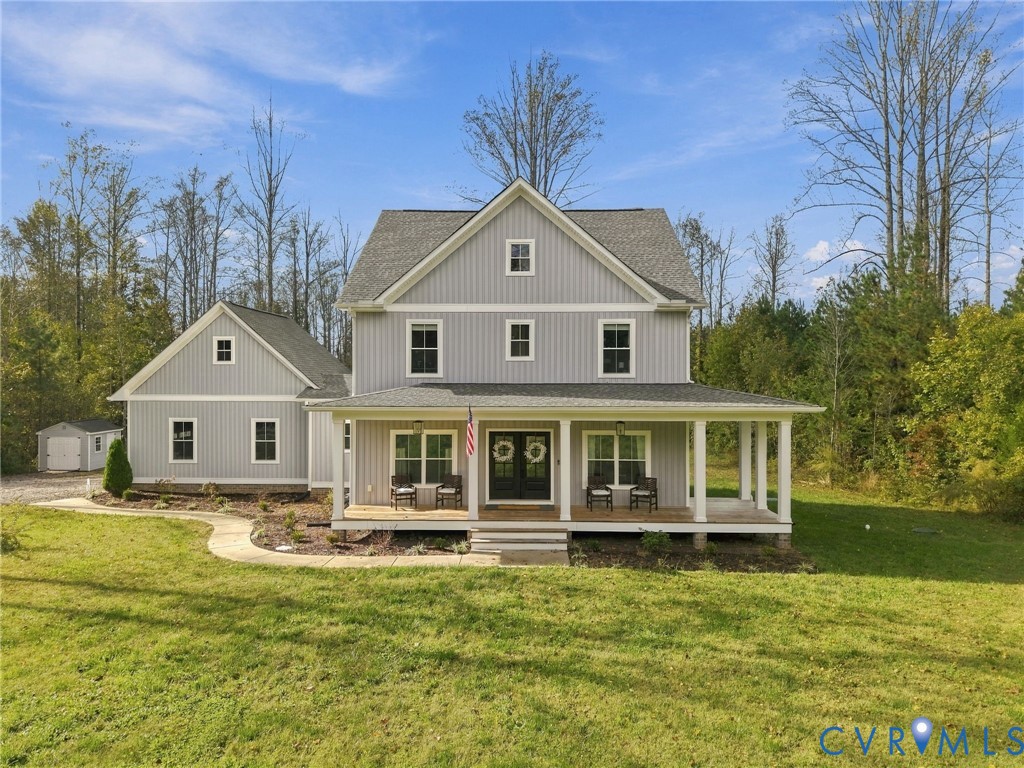 Two-story farmhouse exterior featuring vertical board-and-batten siding, a wraparound covered porch with column supports, a gabled roofline, and a detached outbuilding