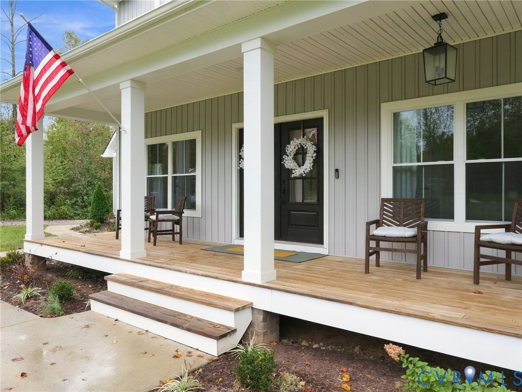 Covered front porch featuring vertical siding, square support columns, wood-finish decking, and a glass-paneled entry door