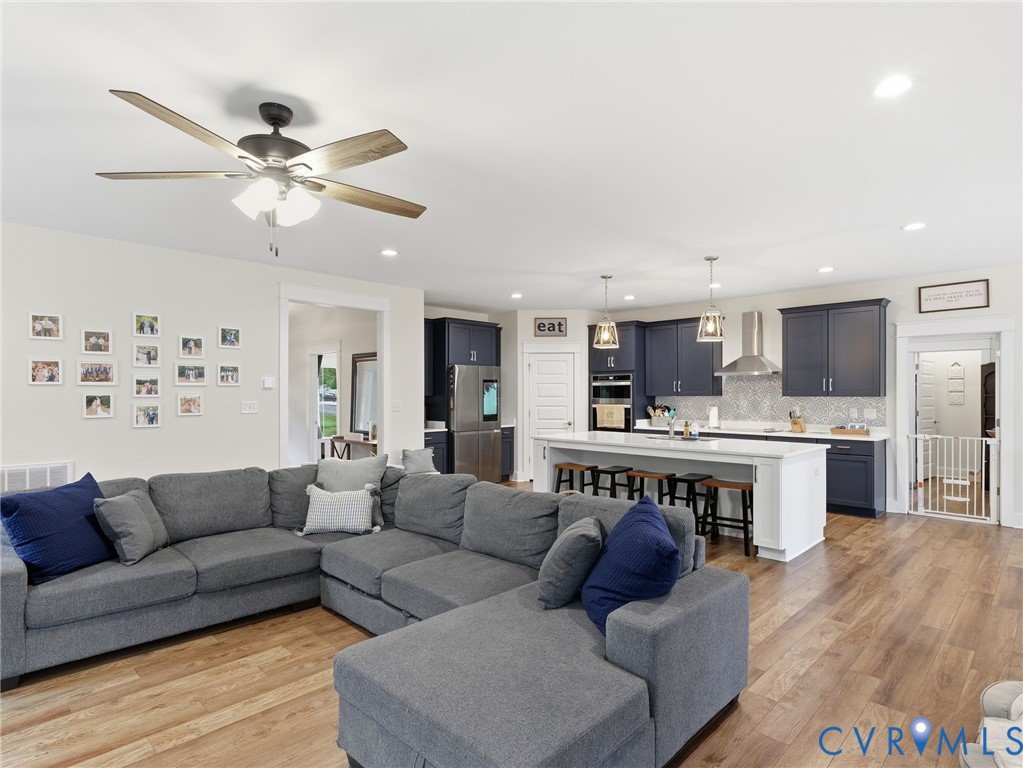 Open-concept kitchen featuring dark cabinetry, a central island with quartz countertop, stainless steel appliances, patterned backsplash tile, and wood-finish flooring
