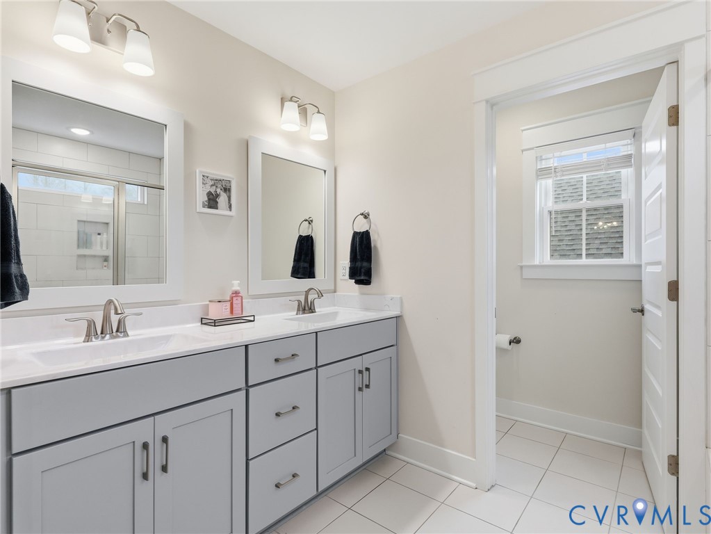 Double vanity featuring gray Shaker-style cabinetry, white countertops, rectangular undermount sinks, and dual-light wall sconces with white glass shades