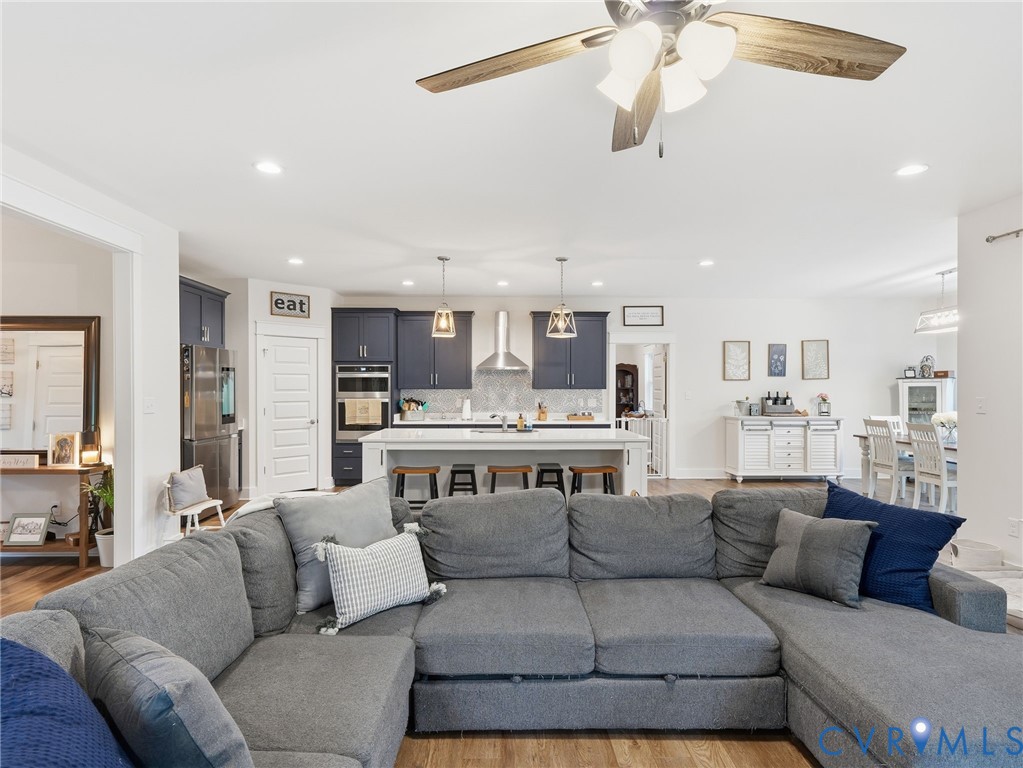 Open-concept kitchen featuring dark-toned cabinetry, a central island with bar seating, stainless steel appliances, a stainless steel range hood, and recessed lighting