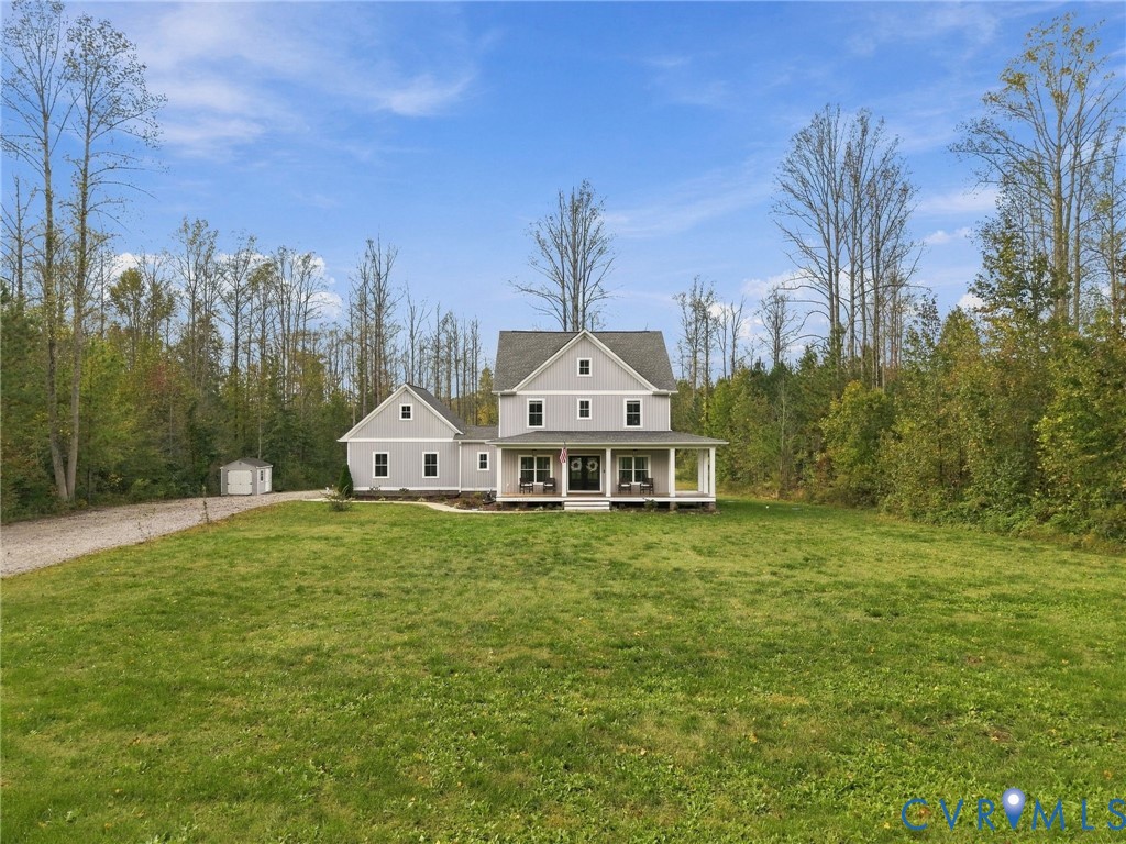 Two-story residence featuring grey lap siding, an expansive covered front porch, asphalt shingle roofing, and a detached storage structure, all situated on a large grassy lot