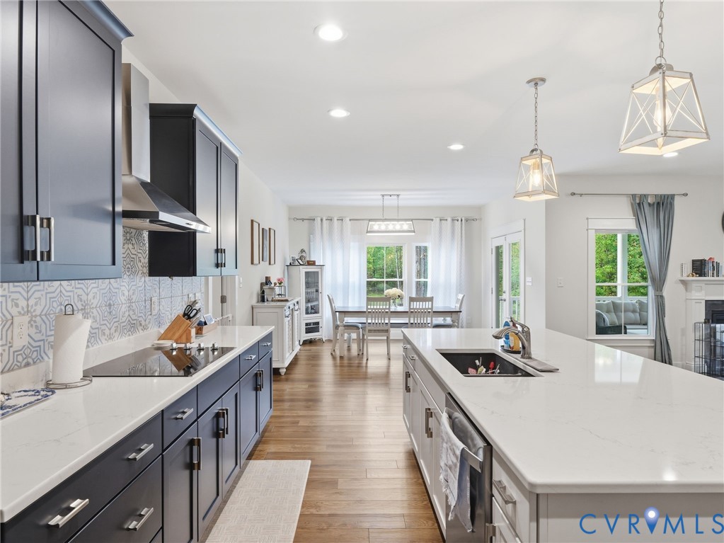 Kitchen featuring dark-toned cabinetry, a spacious center island with a stone-surface countertop, integrated stainless steel appliances, patterned tile backsplash, and wood-finish flooring