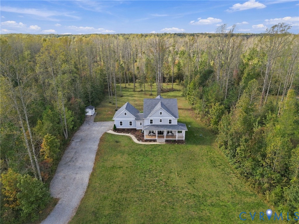 Multi-story residence featuring a covered front porch, light-toned siding, asphalt shingle roof, expansive manicured lawn, and surrounding mature forest