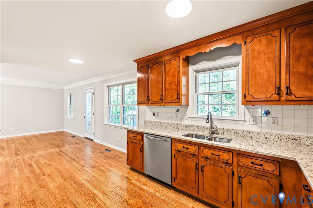 Kitchen featuring wood cabinetry, stone-finish countertops, stainless steel dishwasher, double-basin sink with a high-arch faucet, and wood-finish flooring