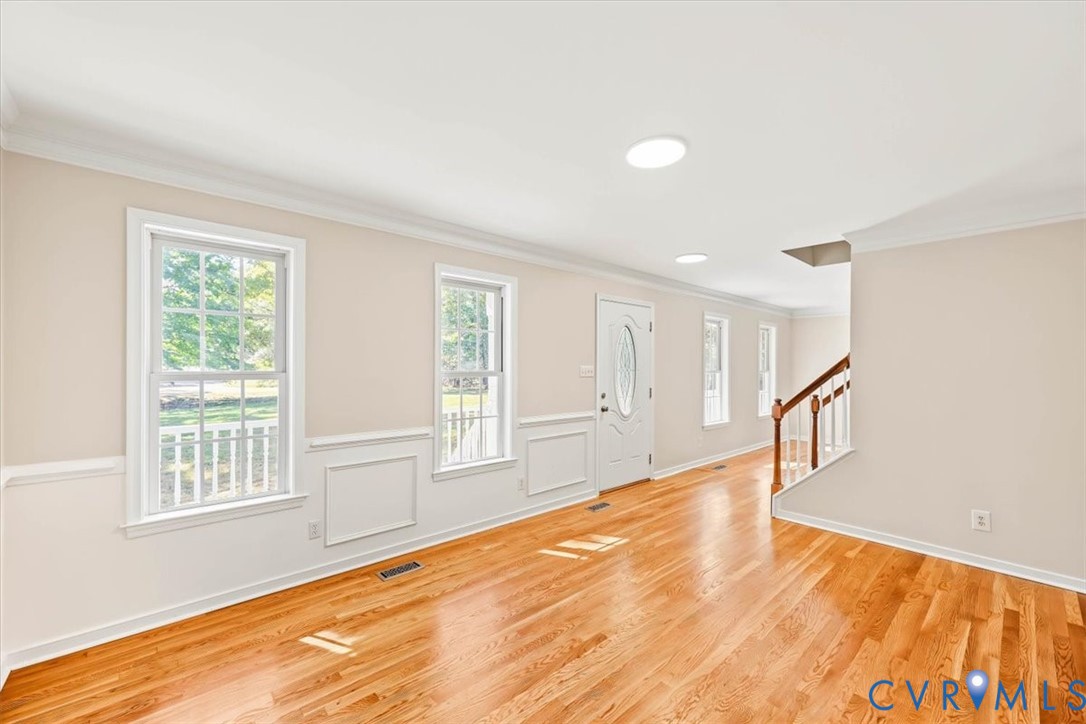 Hardwood flooring, crown molding, chair rail wainscoting, recessed lighting, and a front entry door with an oval glass insert