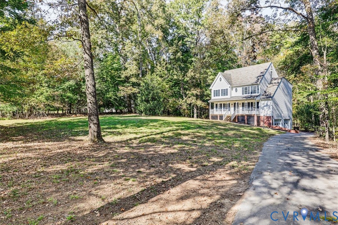 Two-story residence featuring a brick and siding facade, covered front porch, asphalt driveway, and expansive lawn area surrounded by mature trees