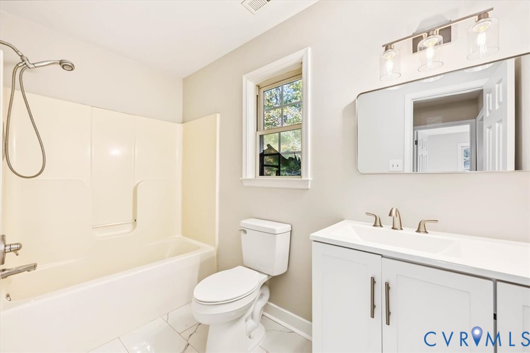 Bathroom featuring a vanity with an integrated sink, polished metal faucet, multi-bulb vanity light, and a tub-shower combination with a handheld sprayer, all finished with light-toned floor tiling