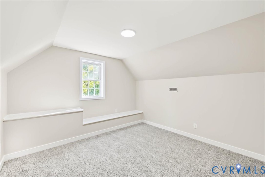 Sloped ceiling architecture featuring neutral carpeting, a double-hung window, and a built-in ledge