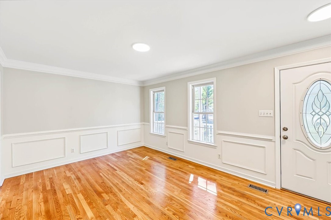 Interior space featuring hardwood flooring, wainscoting, crown molding, double-pane windows, and an entry door with an oval glass insert