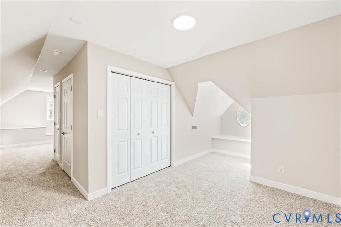 Sloped ceilings with recessed architectural alcove, built-in window seat, oval accent window, neutral carpeting, and double-panel closet doors