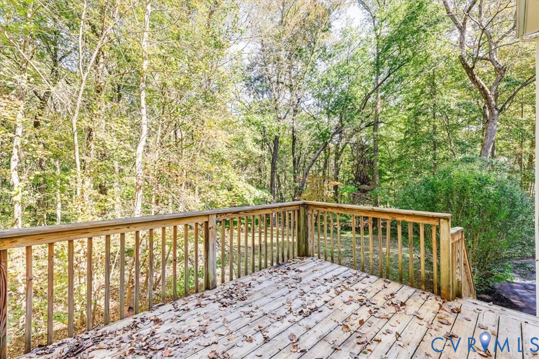 Raised wood deck featuring vertical wood balusters and a wood railing, situated among mature trees