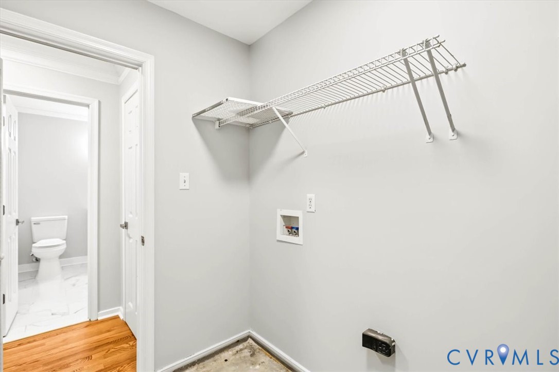 Utility area featuring a wall-mounted wire shelving unit, recessed laundry hookups, and wood-finish flooring