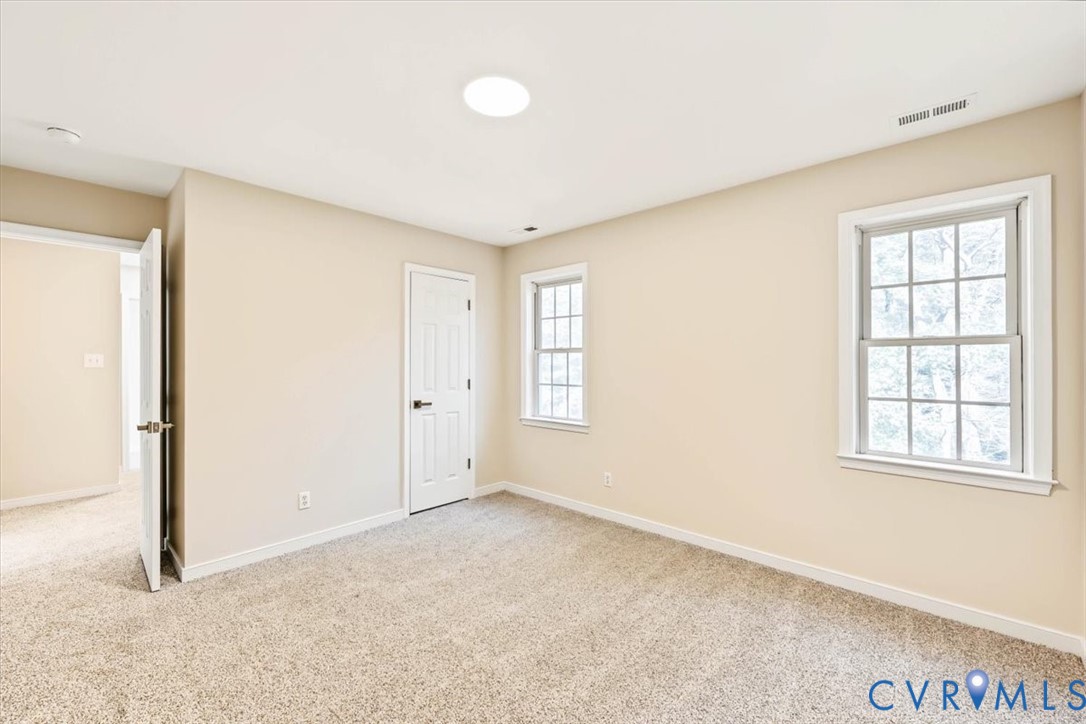 Neutral-toned interior featuring wall-to-wall carpeting, two multi-pane windows, a six-panel door, and a flush-mount ceiling light