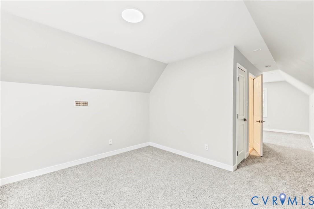 Neutral-toned interior space featuring vaulted ceilings, plush wall-to-wall carpeting, and panel doors with metallic hardware