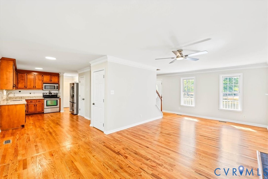 Open-concept interior featuring wood-finish flooring, crown molding, a ceiling fan, and a kitchen equipped with wood cabinetry and stainless steel appliances