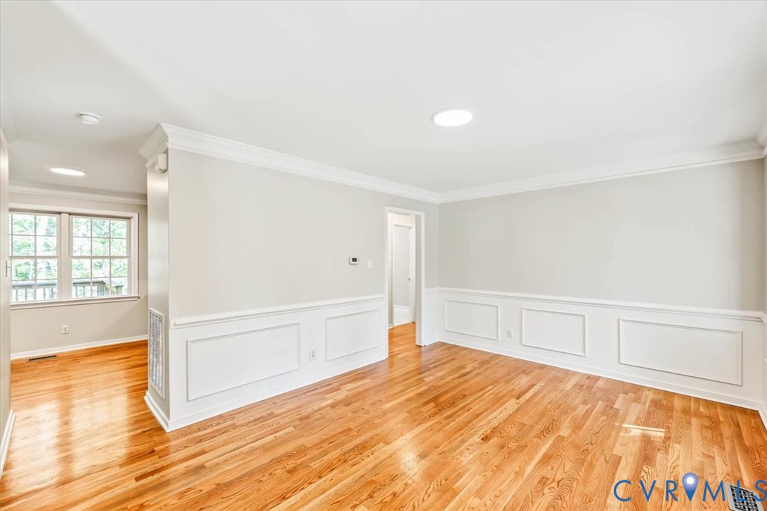 Room featuring wood-finish flooring, white wainscoting, crown molding, and multi-pane windows