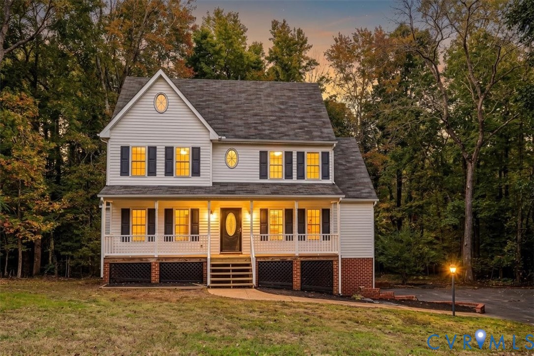 Two-story residence featuring horizontal lap siding, a covered front porch with balustrade railings, decorative oval windows, asphalt shingle roofing, and a brick-faced foundation Two-story residence featuring horizontal lap siding, a covered front porch with balustrade railings, decorative oval windows, asphalt shingle roofing, and a brick-faced foundation