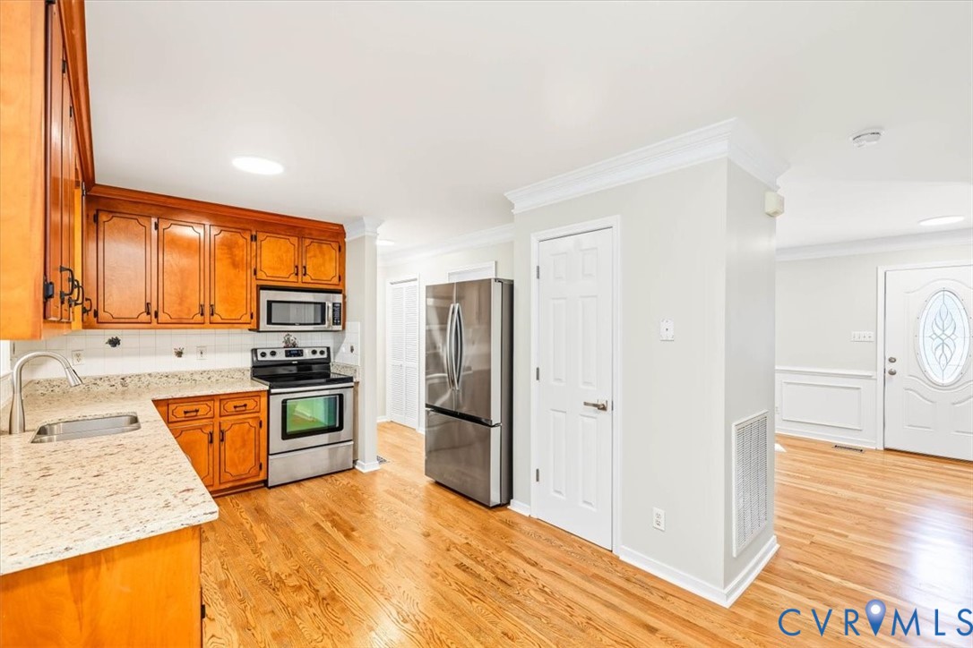 Kitchen featuring natural wood cabinetry, stone-finish countertops, stainless steel appliances, and wood-finish flooring with crown molding