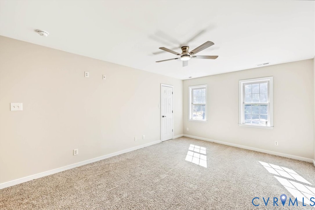 Neutral interior space featuring wall-to-wall carpeting, a multi-blade ceiling fan with integrated lighting, and two double-pane windows with grid mullions