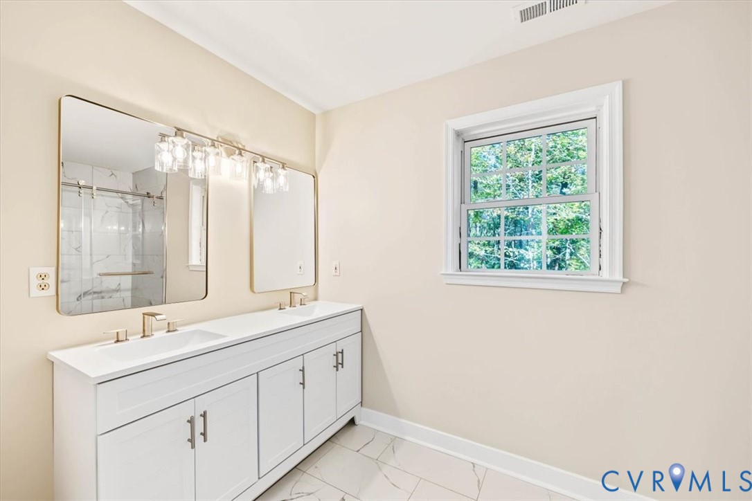 Double vanity with white cabinetry, rectangular under-mount sinks, gold-tone hardware, and an expansive wall-mounted mirror