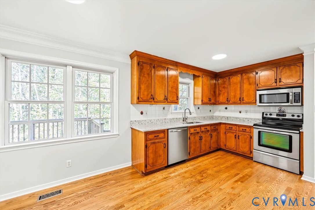 Kitchen featuring wood cabinetry, stone-finish countertops, stainless steel appliances, and wood-finish flooring