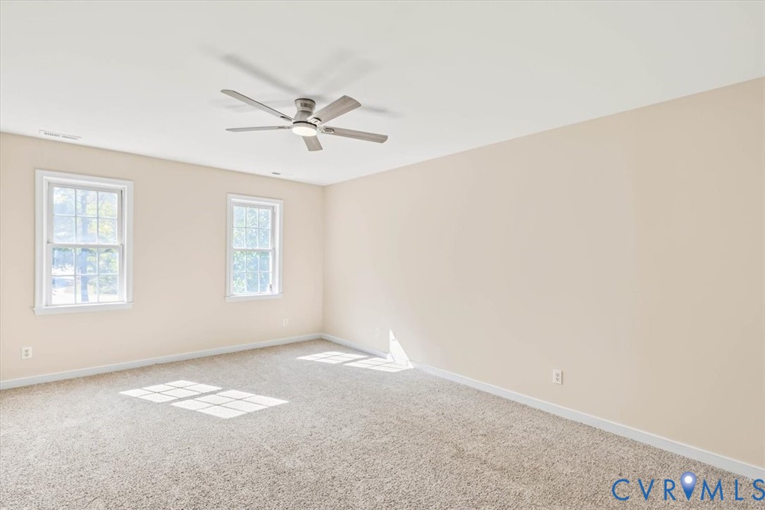 Neutral interior space featuring carpeted flooring, two double-hung windows, and a ceiling fan with integrated lighting