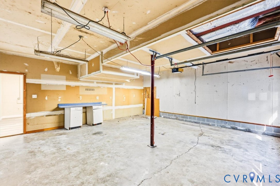Garage interior featuring concrete flooring, a central structural support column, overhead fluorescent lighting, and built-in cabinetry with a laminate countertop