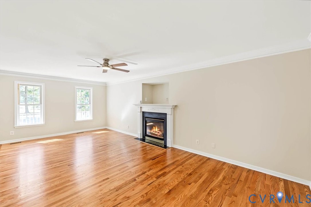 Spacious room featuring wood-finish flooring, a fireplace with a white mantel, crown molding, and a ceiling fan