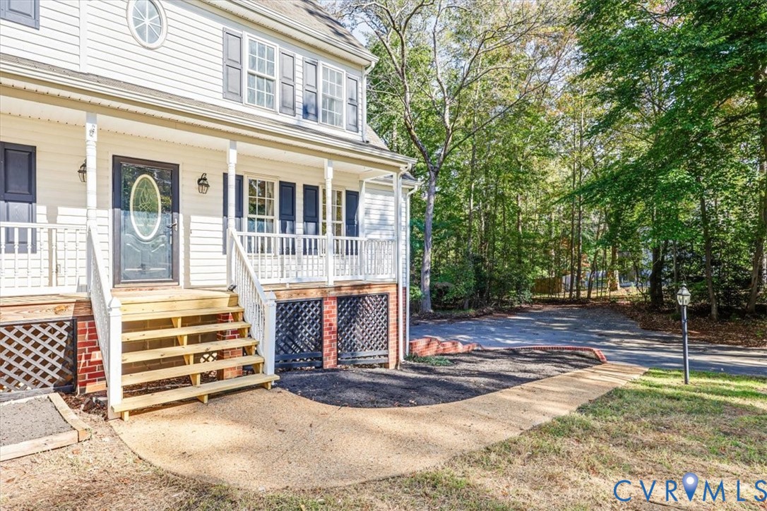 Exterior facade featuring light-colored horizontal siding, a covered front porch with white railing, wood-tone steps, decorative lattice skirting, and an oval-inset entry door
