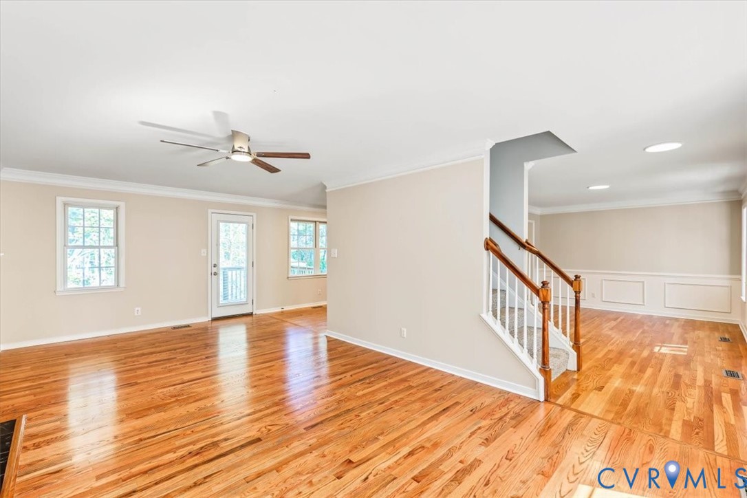 Hardwood flooring, crown molding, ceiling fan with light fixture, staircase with wooden handrail and balusters, and chair rail wainscoting