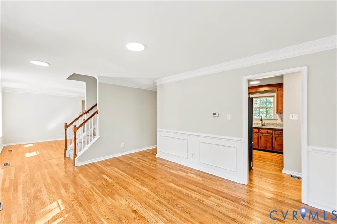 Wood-finish flooring, white wainscoting, crown molding, recessed lighting, and a staircase featuring a wooden handrail with white balusters