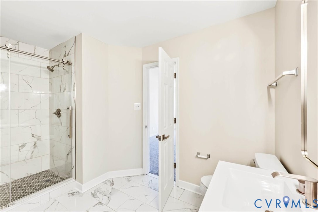 Bathroom featuring a walk-in shower with sliding glass doors and stone-patterned tile, white vanity with integrated sink, and polished metal fixtures