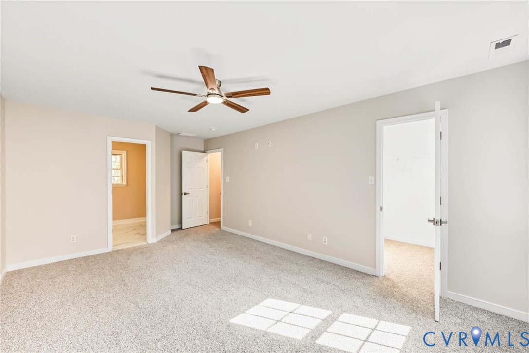 Neutral-toned interior space featuring wall-to-wall carpeting, a ceiling fan with integrated lighting, and multiple interior doorways