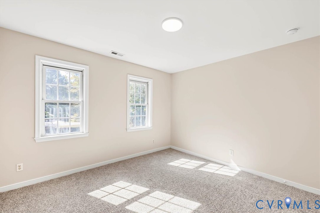 Neutral interior space featuring wall-to-wall carpeting, two double-hung windows, and flush-mount ceiling lighting