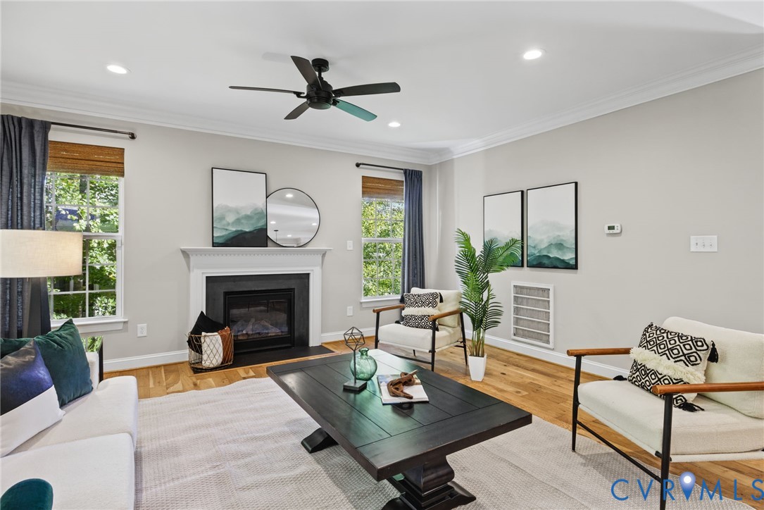 Living area featuring wood-finish flooring, a fireplace with a black surround and mantle, recessed lighting, crown molding, and a central ceiling fan