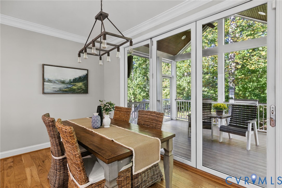 Multi-panel glass doors, wood-finish flooring, crown molding, and a geometric metal chandelier featuring exposed filament bulbs