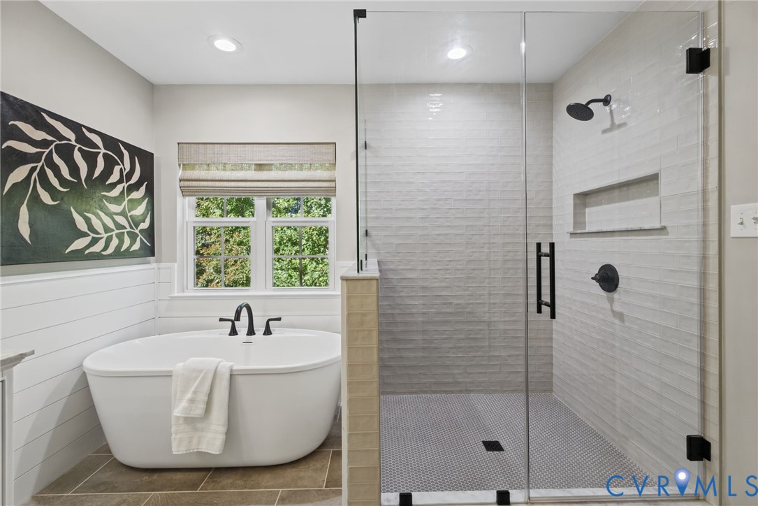 Freestanding soaking tub with matte black faucet, walk-in glass-enclosed shower featuring a recessed wall niche, horizontal shiplap wall paneling, and ceramic tile flooring