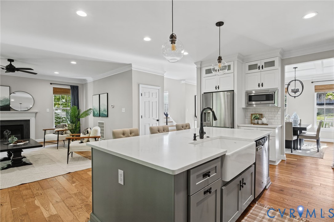 Kitchen featuring an expansive island with a farmhouse-style sink, quartz countertops, stainless steel appliances, white cabinetry, and wood-finish flooring