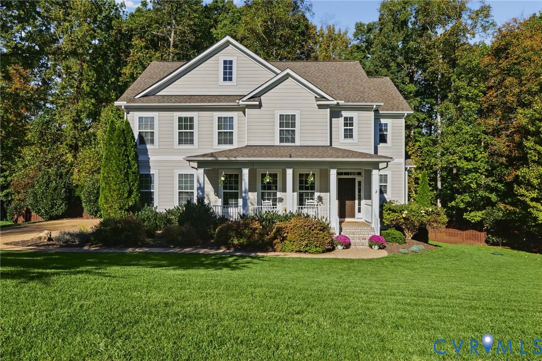 Two-story residence featuring light-toned horizontal siding, a covered front porch with column supports, a gabled roofline, and an expansive lawn