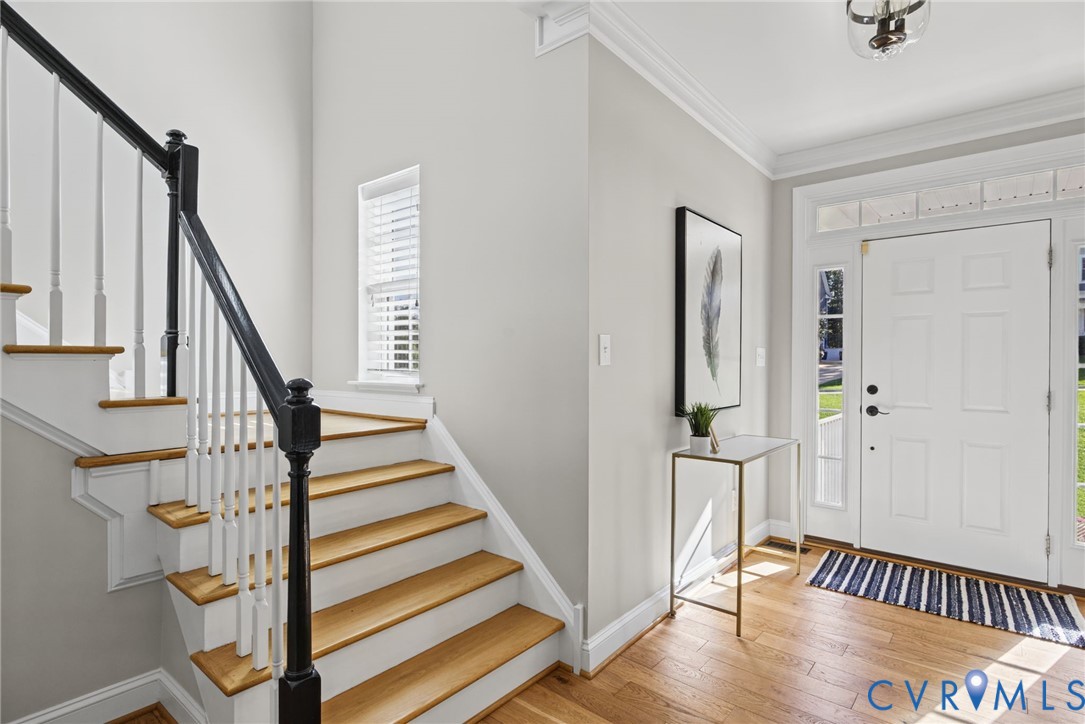 Foyer featuring wood-finish flooring, a six-panel entry door with transom and side light windows, a staircase with a black handrail and white balusters, and crown molding